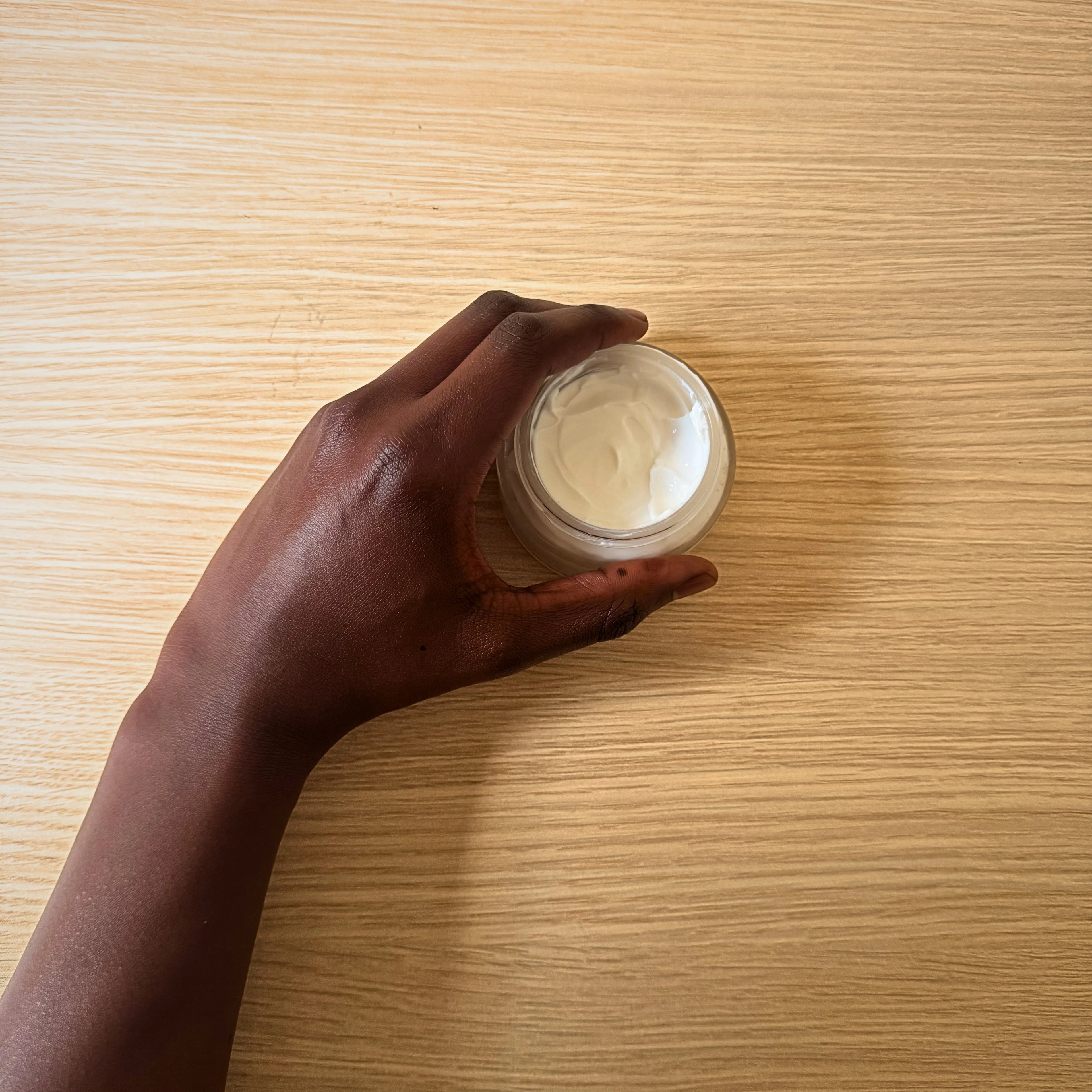 Hand holding a jar of cream on a wooden surface