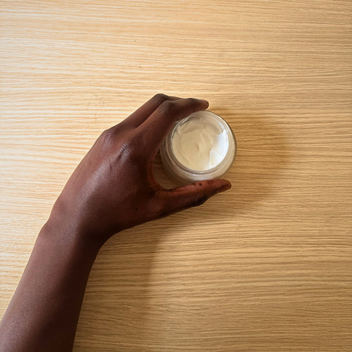 Hand holding a jar of cream on a wooden surface