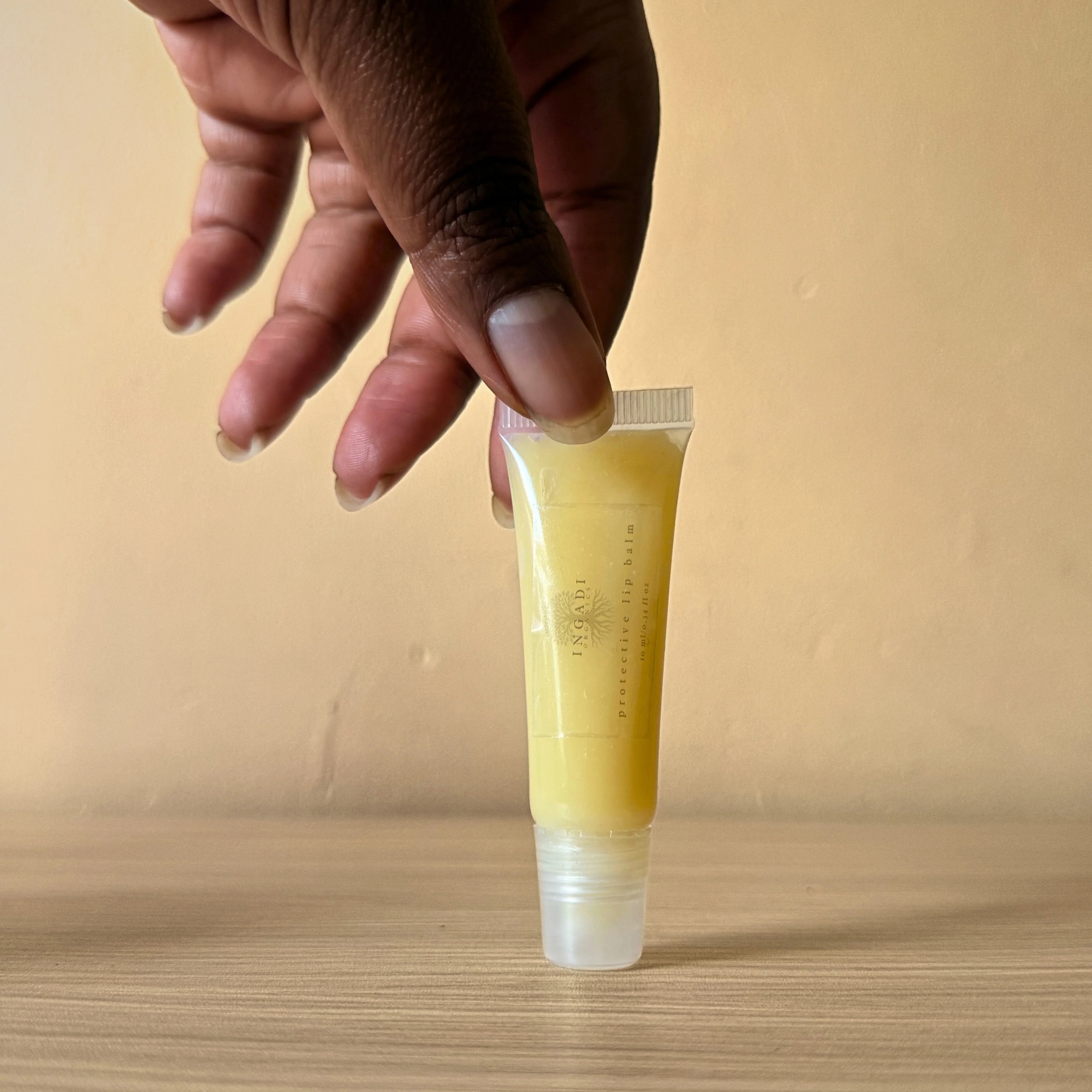Hand holding a tube of yellow lip balm against a beige background