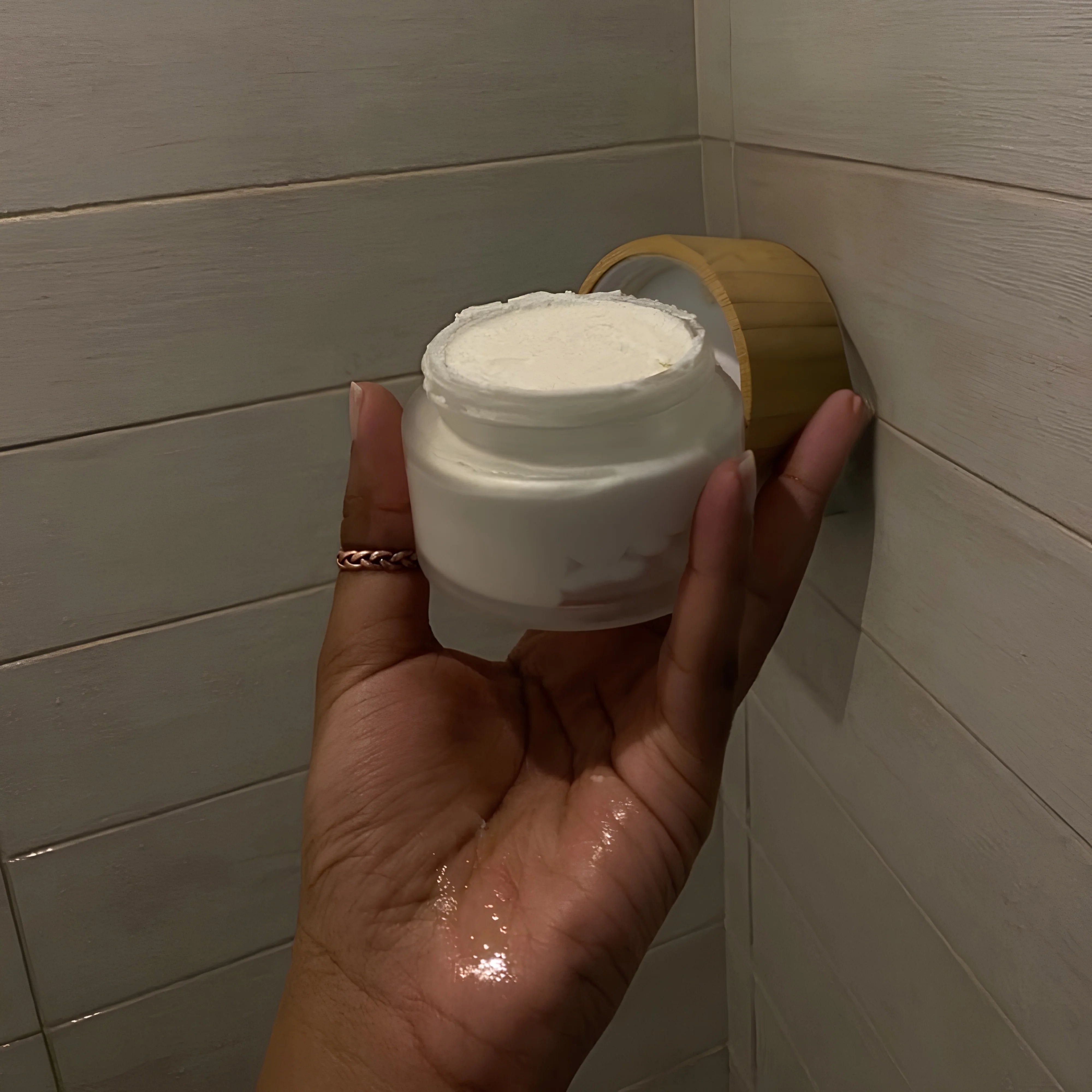 Hand holding a white jar against a tiled bathroom wall