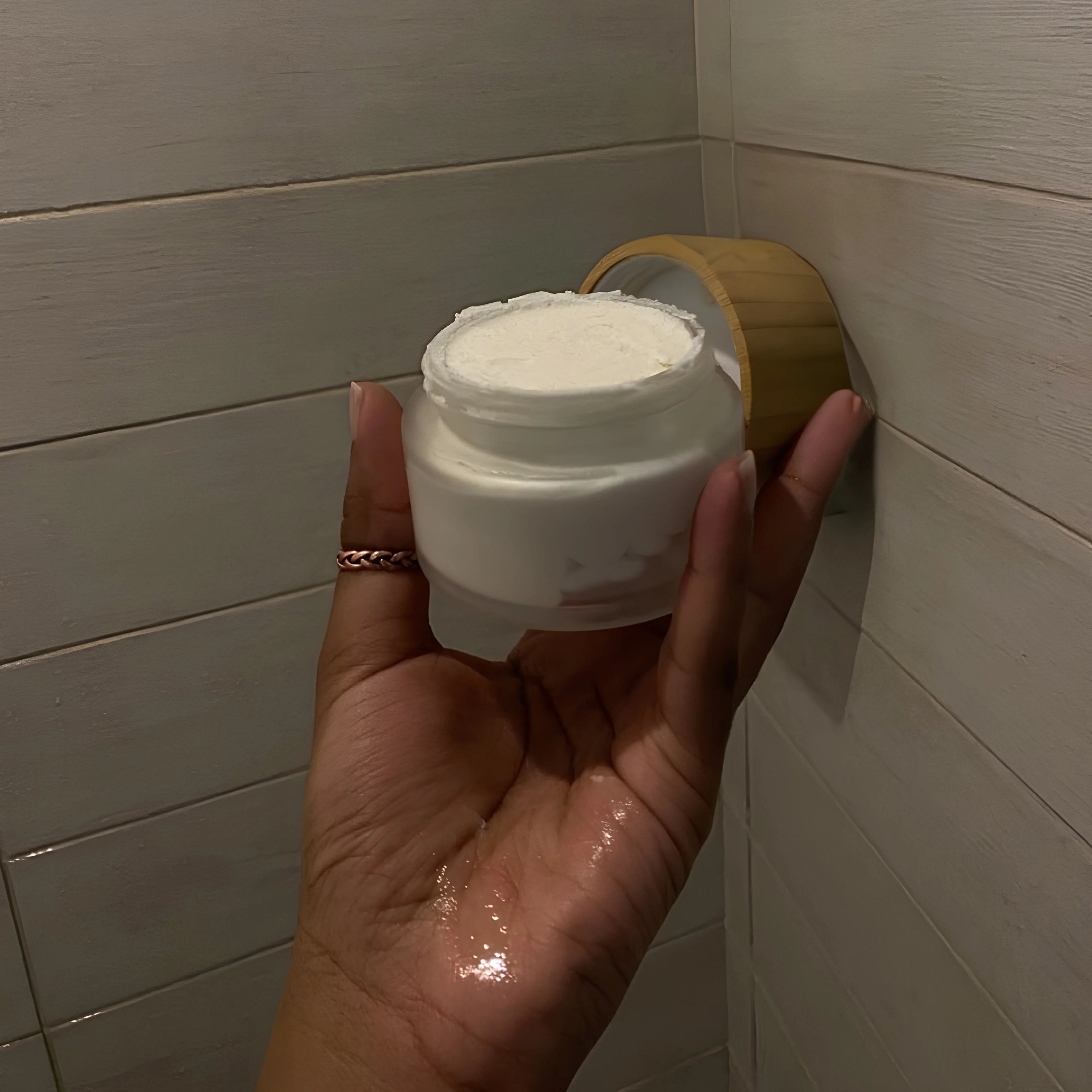 Hand holding a white jar against a tiled bathroom wall